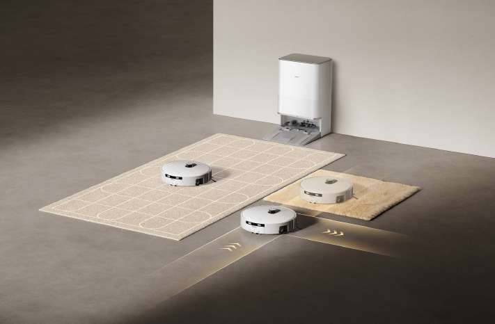 Trois aspirateurs robots Xiaomi sur un sol dur et des tapis, avec leur station